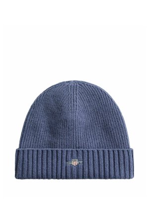 Bonnet en maille bleu foncé avec bord replié présentant une petite étiquette rectangulaire avec un logo en forme de bouclier au centre devant.