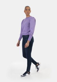 Levendula színű pulóver puffos ujjal, sötét, slim fit farmernadrággal és színes sportcipőkkel párosítva. Sima anyag és testhez álló fazon.
