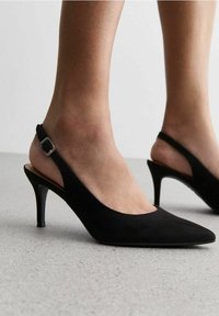 Tacchi slingback in suede nero con punta affusolata e tacco sottile. Presentano una fascia alla caviglia regolabile e una texture liscia.