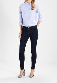 Hellblau gestreiftes Hemd mit Knöpfen, dunkle Skinny Jeans und silberne High Heels. Das Hemd hat einen Kragen und hochgekrempelte Ärmel.