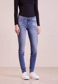 Slim-fit blå denimjeans med blekning, framfickor och knappstängning, ihop med en svart långärmad topp och vita sneakers.