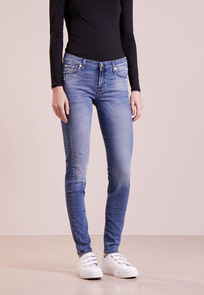 Slim-fit blå denimjeans med blekning, framfickor och knappstängning, ihop med en svart långärmad topp och vita sneakers.