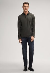 Polo a maniche lunghe verde scuro con colletto, caratterizzato da un logo discreto. Abbinato a un paio di jeans in denim scuro e scarpe in pelle nere.