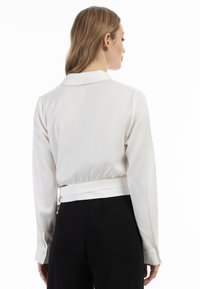 Hvid cropped bluse med klassisk krave og lange ærmer, der har en indsnævret talje og knapmanchetter. Glat, letvægtsstof.