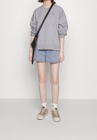 Šedá mikina s logem, světle modré džíny, béžové tenisky a bílé ponožky s černým logem. Ukázkový neformální outfit.