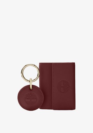 Burgundy leather wallet with embossed logo, accompanied by a round keychain with a metallic ring. Smooth texture, minimalist design.