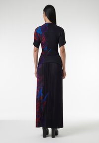 Top de punto con manga corta en un patrón abstracto negro y rojo-azul; falda larga plisada en negro sólido. Textura suave, diseño ajustado.