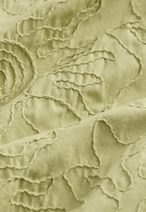 Un tessuto verde chiaro presenta un ricamo testurizzato con motivi a spirale e curvi, che conferiscono profondità e interesse tattile al materiale.