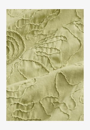 Light green fabric features textured embroidery with swirling and curved patterns, adding depth and tactile interest to the material.