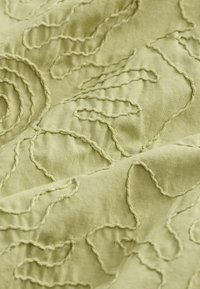 Lichtgroene stof met een gestructureerd, verhoogd borduurwerk met draaiende bloemmotieven, met een gladde, zachte afwerking.
