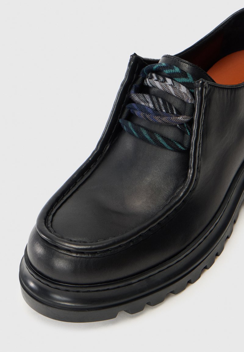 Sorte lædersko med en afrundet tå, syninger og tekstureret sål. Snørebåndene har et blåt og gråt stribet mønster.