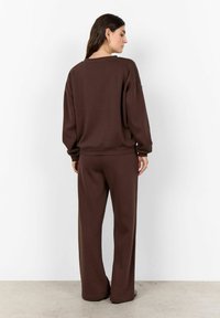 Bruine oversized sweatshirt met verlaagde schouders, gecombineerd met bijpassende wijde broek. Zacht materiaal met een gladde textuur, minimale details.