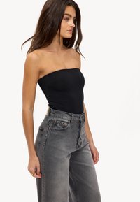 Bodysuit noir sans bretelles associé à un jean large taille haute en gris délavé. Le jean présente une fermeture à boutons et des accents en métal couleur cuivre.