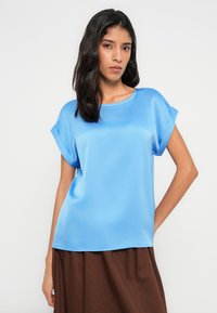 Světle modrý saténový top s krátkými rukávy a kulatým výstřihem. Hladká textura a volný střih, doplněný hnědou texturovanou sukní.