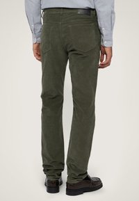 Oliwkowe spodnie sztruksowe o dopasowanym kroju, z tylnymi kieszeniami i teksturowaną powierzchnią, połączone z ciemnymi butami wsuwanymi.