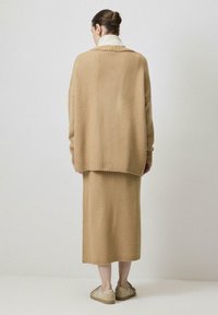 Beige, oversized pulóver és a hozzáillő, puha kötött anyagból készült szoknya. Bordázott élek és kényelmes, laza fazon jellemzi. A szettet hétköznapi lábbeli egészíti ki.