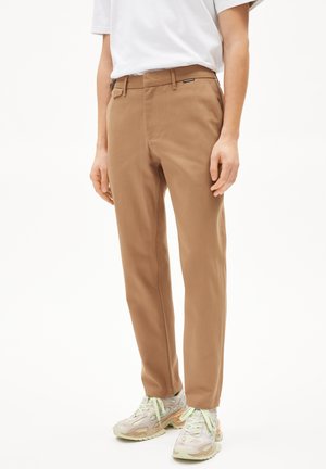 Beige Hosen mit geradem Bein, ausgestattet mit Gürtelschlaufen, Taschen vorne und einer glatten Textur, kombiniert mit weißen Sneakers.