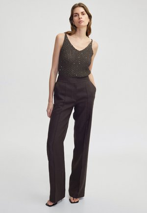 Brown wide-leg trousers with front pleats, paired with a dark knitted top featuring a V-neck and textured pattern. Simple black sandals.