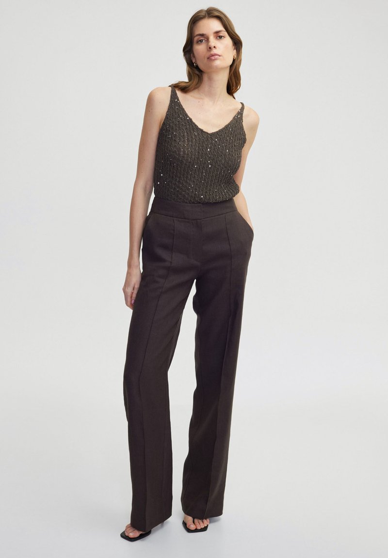 Bruine wijde broek met voorplooien, gecombineerd met een donker gebreid top met een V-hals en een textuurpatroon. Eenvoudige zwarte sandalen.