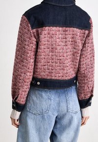 Chaqueta recortada con una tela tejida texturizada en tonos rosa y rojo, con acentos de mezclilla azul oscura. Dos botones a presión en la parte delantera en la cintura.