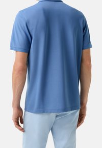 Polo bleu clair, manches courtes, col classique, texture lisse et fentes sur les côtés à l'ourlet. Le pantalon est bleu clair, créant un look coordonné.