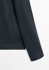 Poignet de chemise à manches longues bleu marine foncé avec coutures visibles sur fond blanc uni.