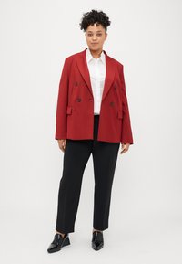 Raudona dviguba švarko blazer, su didelėmis juodomis sagomis, derinama su balta marškiniais ir juodomis kelnėmis. Pasižymi laisvu kirpimu ir ilgomis rankovėmis.