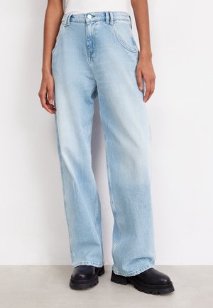 Jeans de mezclilla azul claro, de pierna ancha y cintura alta, con dos bolsillos delanteros y cierre de botón, combinados con botines negros gruesos.