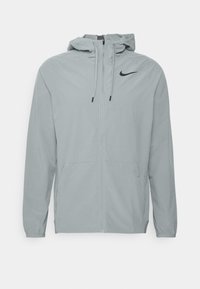 Světle šedá nike bunda s kapucí, předním zipem, elastickými manžetami a dvěma bočními kapsami. Na hrudi je černé logo svíčkového swoosh.