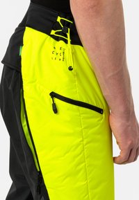 Zwarte en neongele knielange broek met meerdere zakken, textuurstof, een trekkoordtaille en branding van gerecycled materiaal.