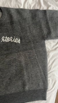 Szürke pulóver puha anyagból, bordázott nyakkivágással és szegéllyel. Az elején fehérrel hímzett "Stories" felirat található.