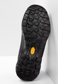 Black rubber shoe sole with deep tread patterns, featuring a yellow Vibram logo, designed for grip and durability.