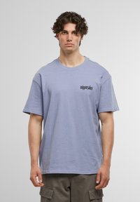 Tricou de culoare violet deschis, cu mâneci scurte, având un mic logo negru pe partea stângă a pieptului. Material moale, croi lejer, decolteu rotund.