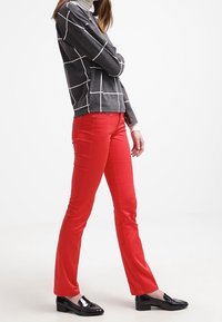 Top gris de manga larga con un patrón de cuadrícula blanca combinado con pantalones rectos rojos y mocasines de charol negros.