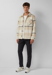 Geruite jas in beige, crème en grijs wolmengsel met een knoopsluiting en een enkele borstzak; gecombineerd met donkere broek en sneakers.