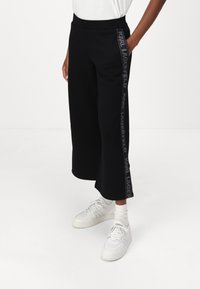 Fekete, bő szárú melegítőnadrág, kényelmes, rugalmas derékrésszel és oldalpanellel, amelyen reflektáló "Karl Lagerfeld" logo részlet található.