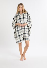 Flanellen poncho in een crème- en zwart geruit patroon. Voorzien van een capuchon en losse mouwen, reikt tot halverwege de dij. Zachte textuur en warme uitstraling.