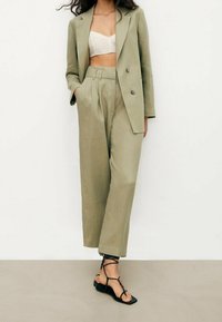 Olive green linen suit set featuring a double-breasted blazer and pleated wide-leg trousers, paired with black strappy sandals.