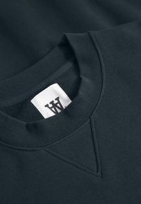 Dark navy sweatshirt featuring a ribbed crew neckline, a triangular reinforce stitch, and a white label with a logo inside the collar.
