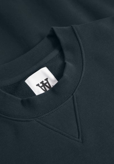 Sweatshirt bleu marine foncé avec un col ras du cou côtelé, une couture de renfort triangulaire et une étiquette blanche avec un logo à l'intérieur du col.