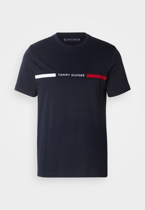 Sötétkék pamut póló kerek nyakkal. Fehér és piros vízszintes csíkok a mellrészen. A "TOMMY HILFIGER" logó kontrasztos fehér színű betűvel.