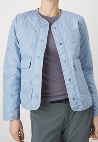Jasnoniebieska pikowana kurtka z okrągłym dekoltem, zatrzaskami, dwiema przednimi kieszeniami oraz logo na piersi. Wykonana z gładkiego materiału.