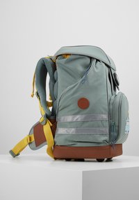 Sac à dos en tissu vert avec accents jaunes, design structuré, bretelles rembourrées, poche latérale, et détails décoratifs avec badge et écusson.