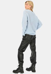 Jasnoniebieski sweter z dzianiny, czarne spodnie z ekoskóry oraz czarne, sznurowane buty z łańcuchowym akcentem. Miękka tekstura, luźny krój, nowoczesny design.