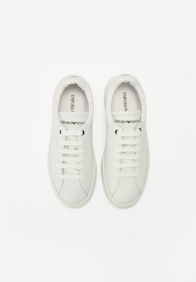 Hvite lær sneakers med rund tå, flate hvite lisser, subtile perforeringer og logo på tungen, med glatt tekstur og minimalistisk design.