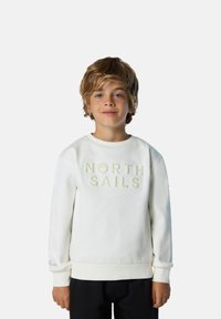 Sudadera blanca con la inscripción "NORTH SAILS" en letras en relieve, puños y dobladillo acanalados. Textura suave con un corte relajado, combinada con pantalones negros.