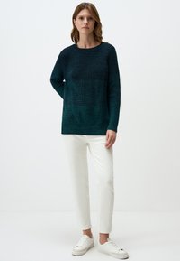 Gebreide teal trui met een ronde hals en geribde mouwen, gecombineerd met witte slim-fit broek en witte sneakers. Gladde textuur en ontspannen pasvorm.