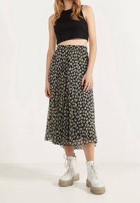 Top corto negro combinado con una falda midi con pliegues que presenta un patrón floral amarillo y blanco sobre un fondo negro. Botas de combate blancas.