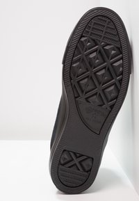 Černá podrážka tenisky Converse All Star s texturovaným geometrickým vzorem, nakloněná proti bílému pozadí.