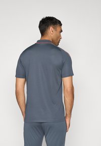 Grå polo t-shirt lavet af glat stof, med en klassisk krave og kontrastfarvede røde detaljer langs skuldrene. Kortærmet, afslappet pasform.